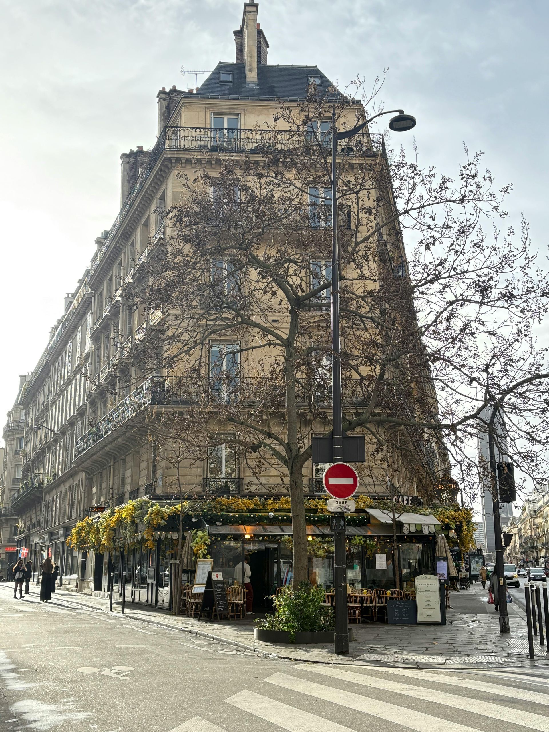 Immeuble d'angle à Paris avec un restaurant ; arbre devant et panneau « Sens interdit ».