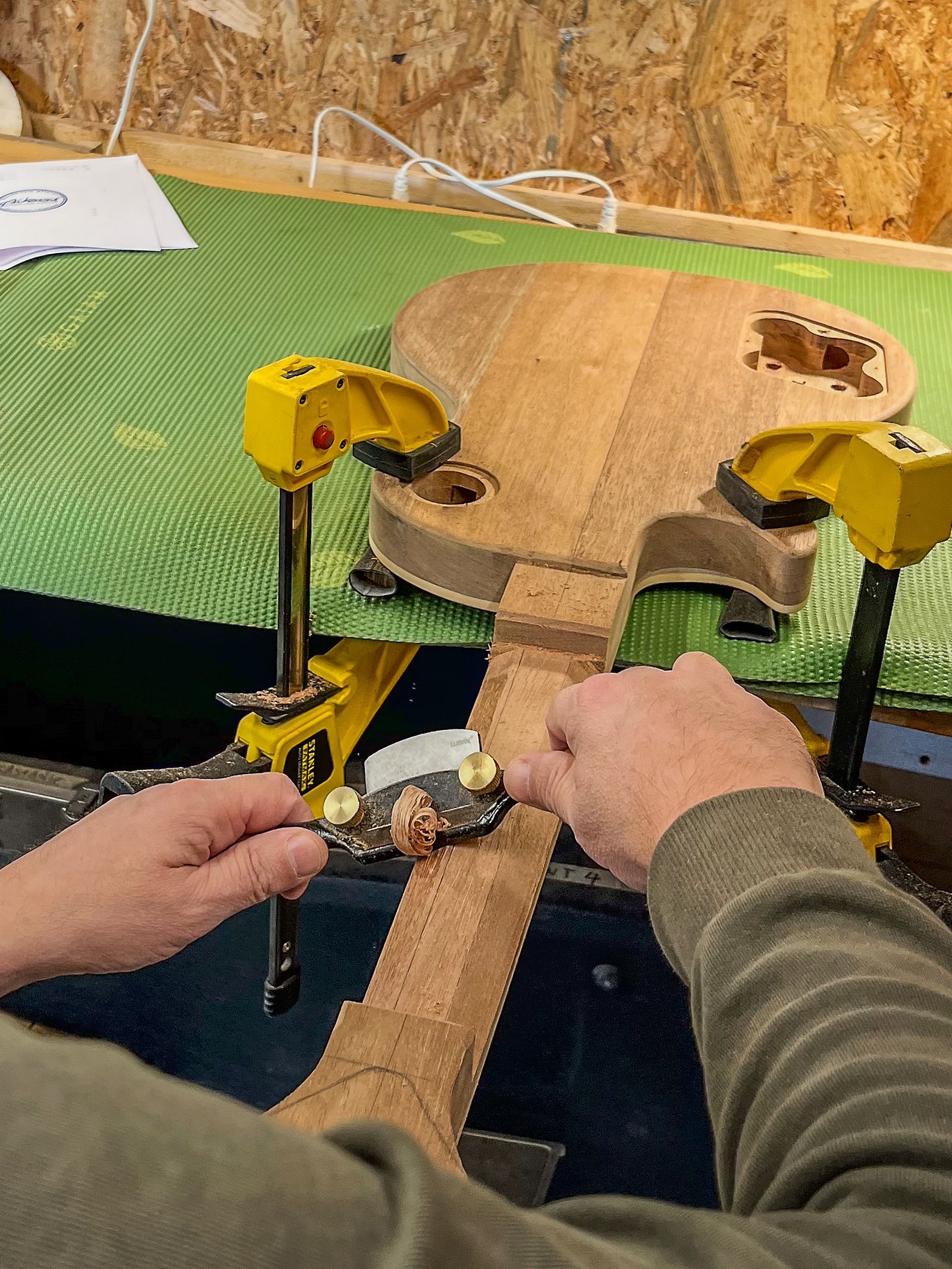Iemand werkt in een werkplaats aan een gitaar. Gitaar nek shaping. Handgemaakte gitaar. Art of Noise Guitars