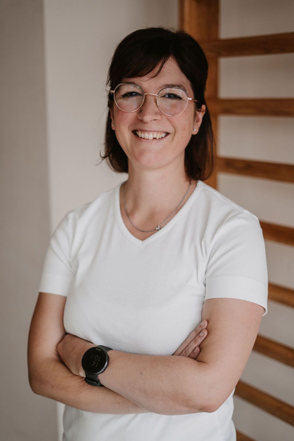 Eine Frau mit Brille und weißem Hemd lächelt und verschränkt die Arme.
