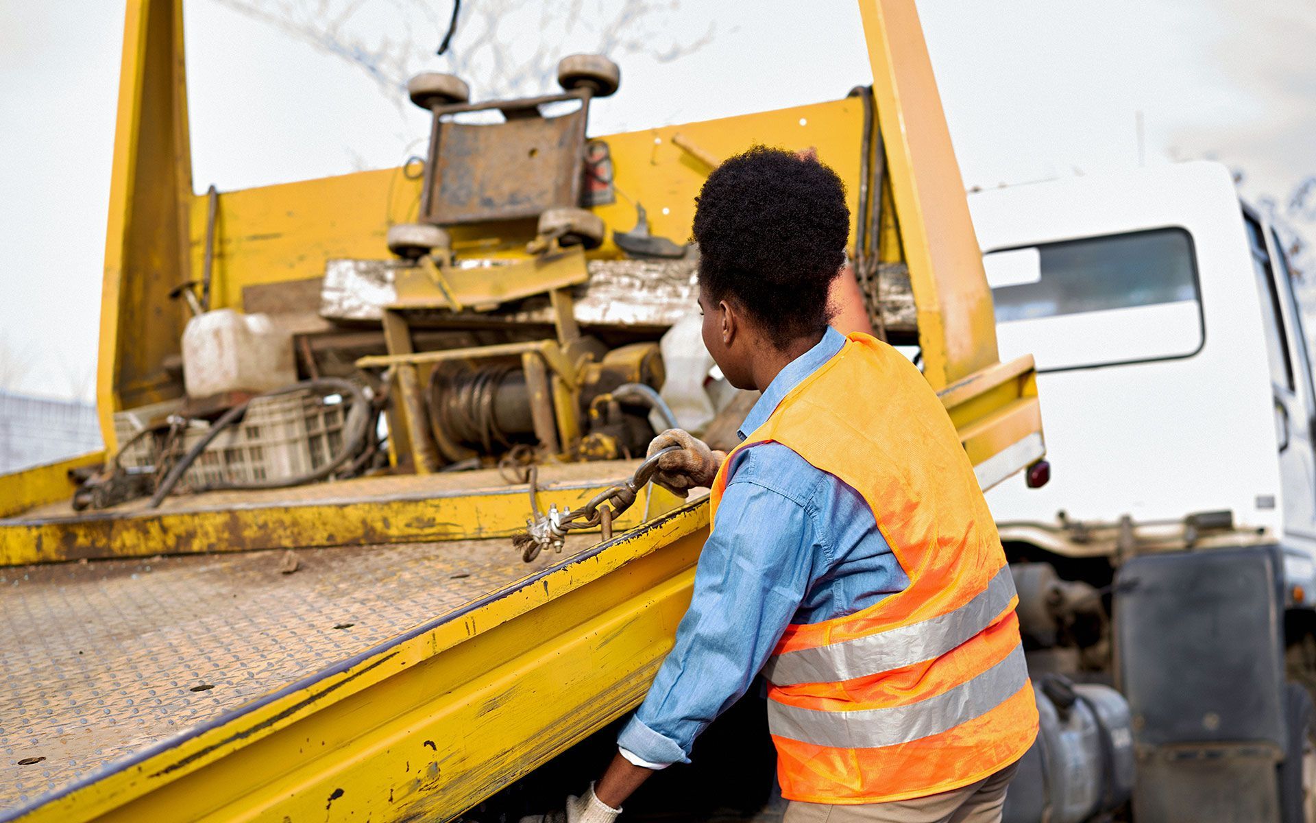 A man in an orange vest is working on a tow truck.