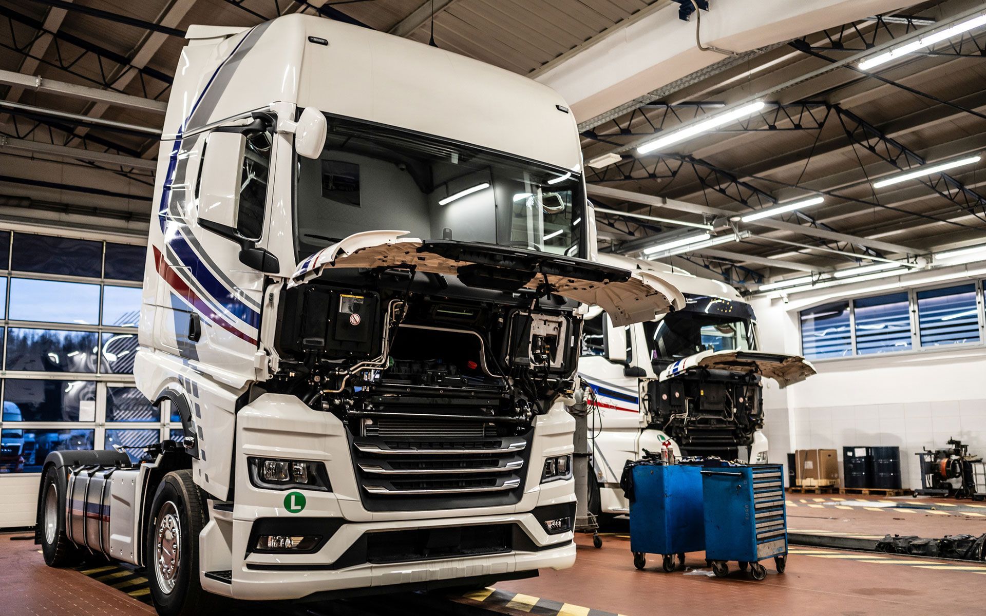 A truck is being repaired in a garage with its hood open.