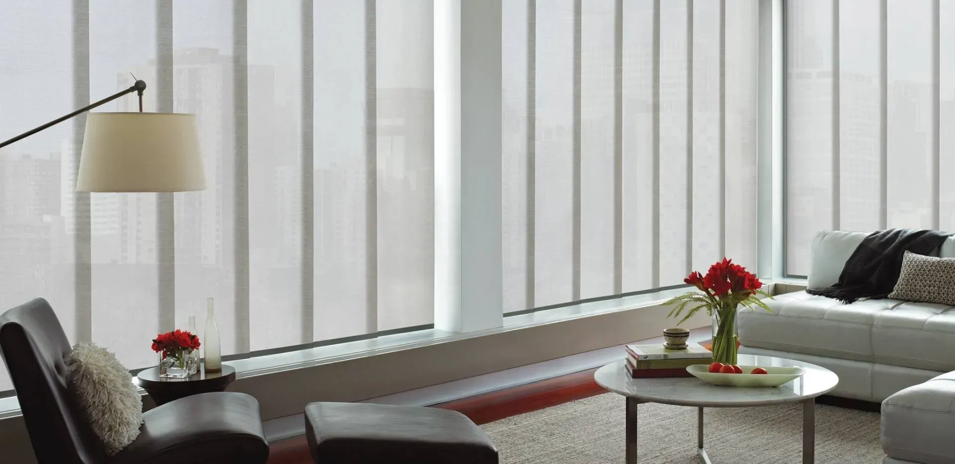 Living room with light-colored vertical blinds, leather chair, sofa, and round coffee table.