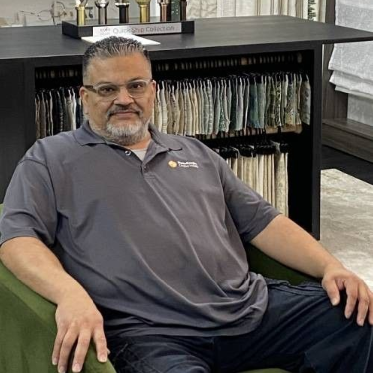 Man in gray shirt seated in a green chair, in front of fabric samples.