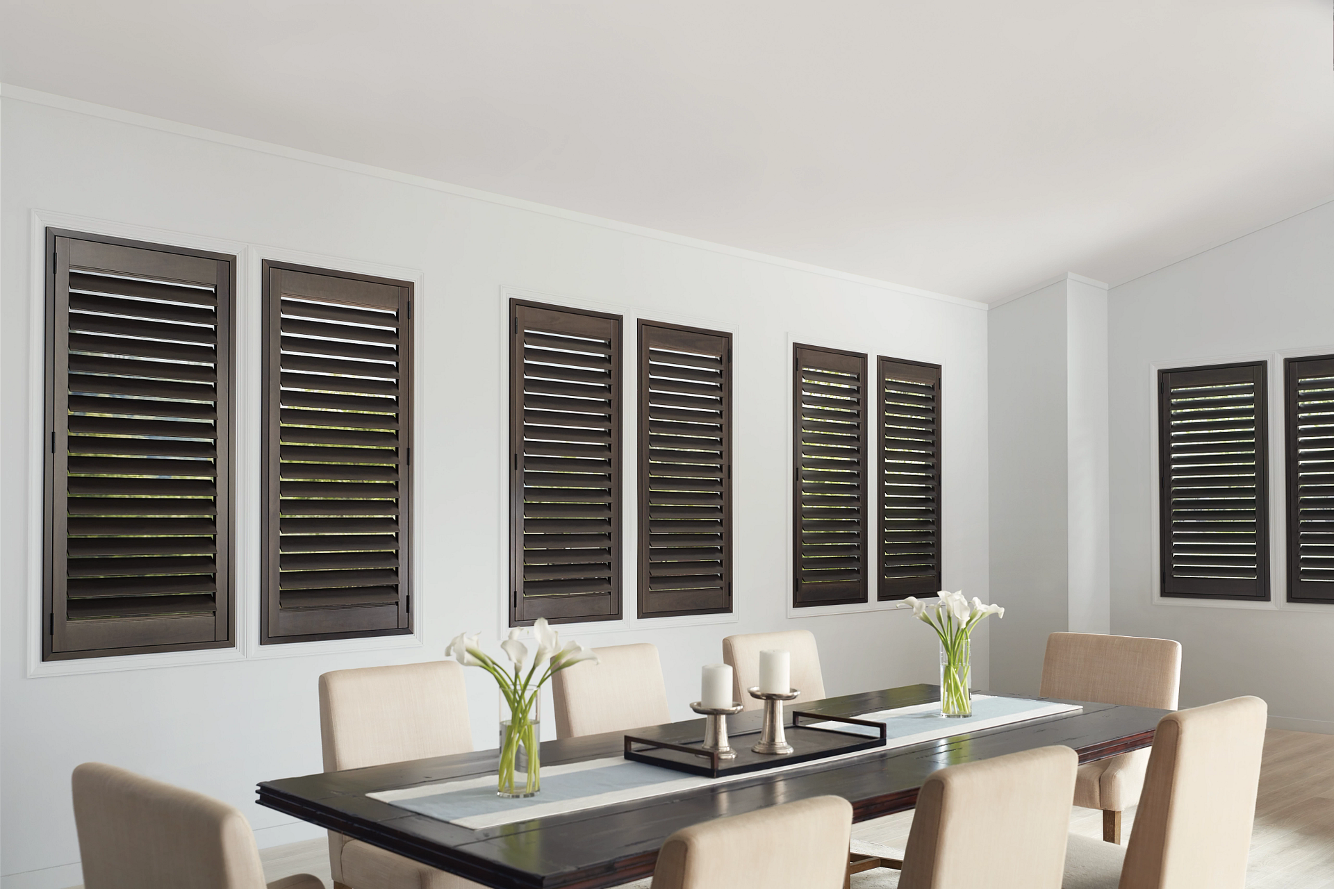 Dining room with dark brown shutters on white walls, over a table set for dining.