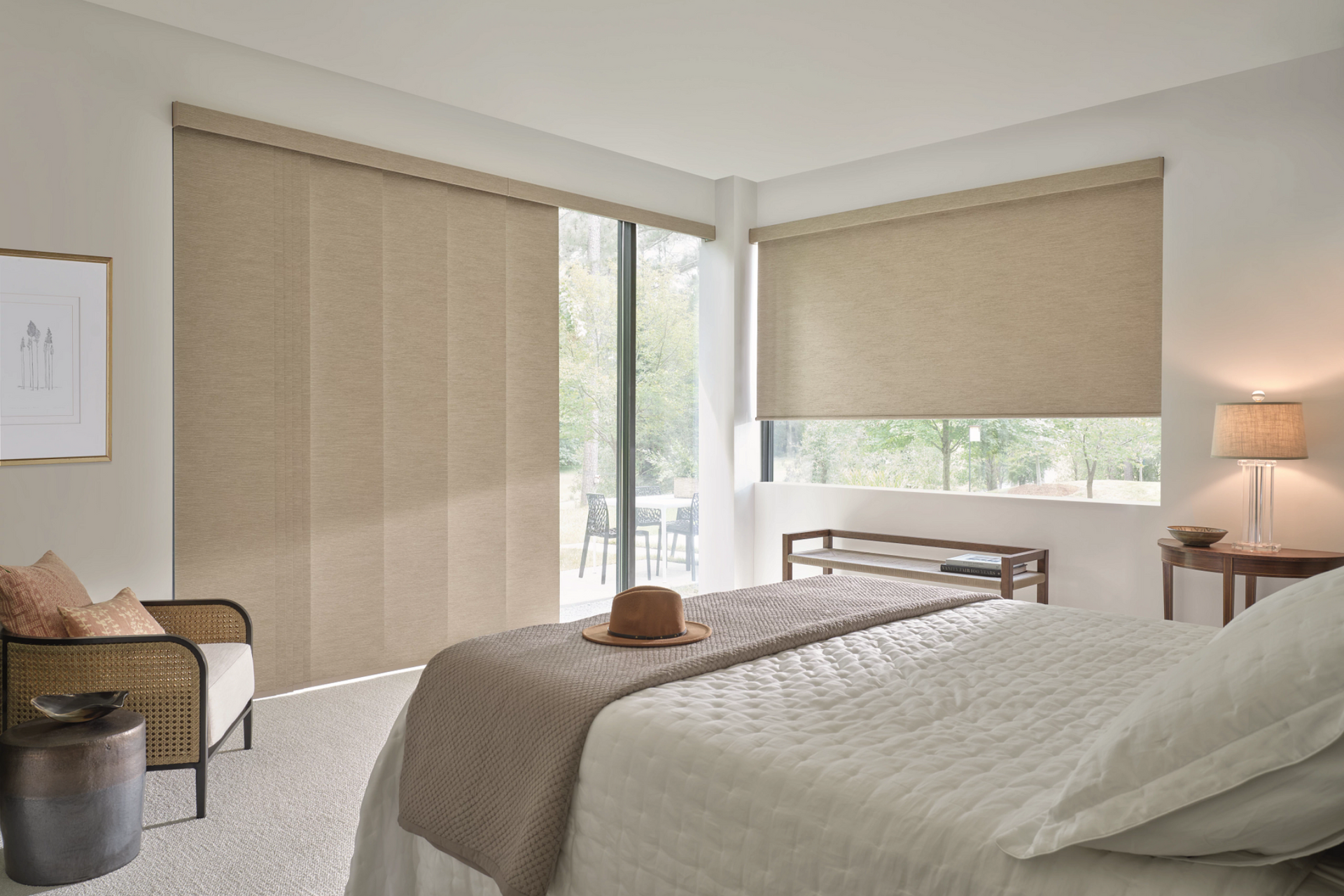 Bedroom with beige panel track blinds, roller shade, bed, and chair.