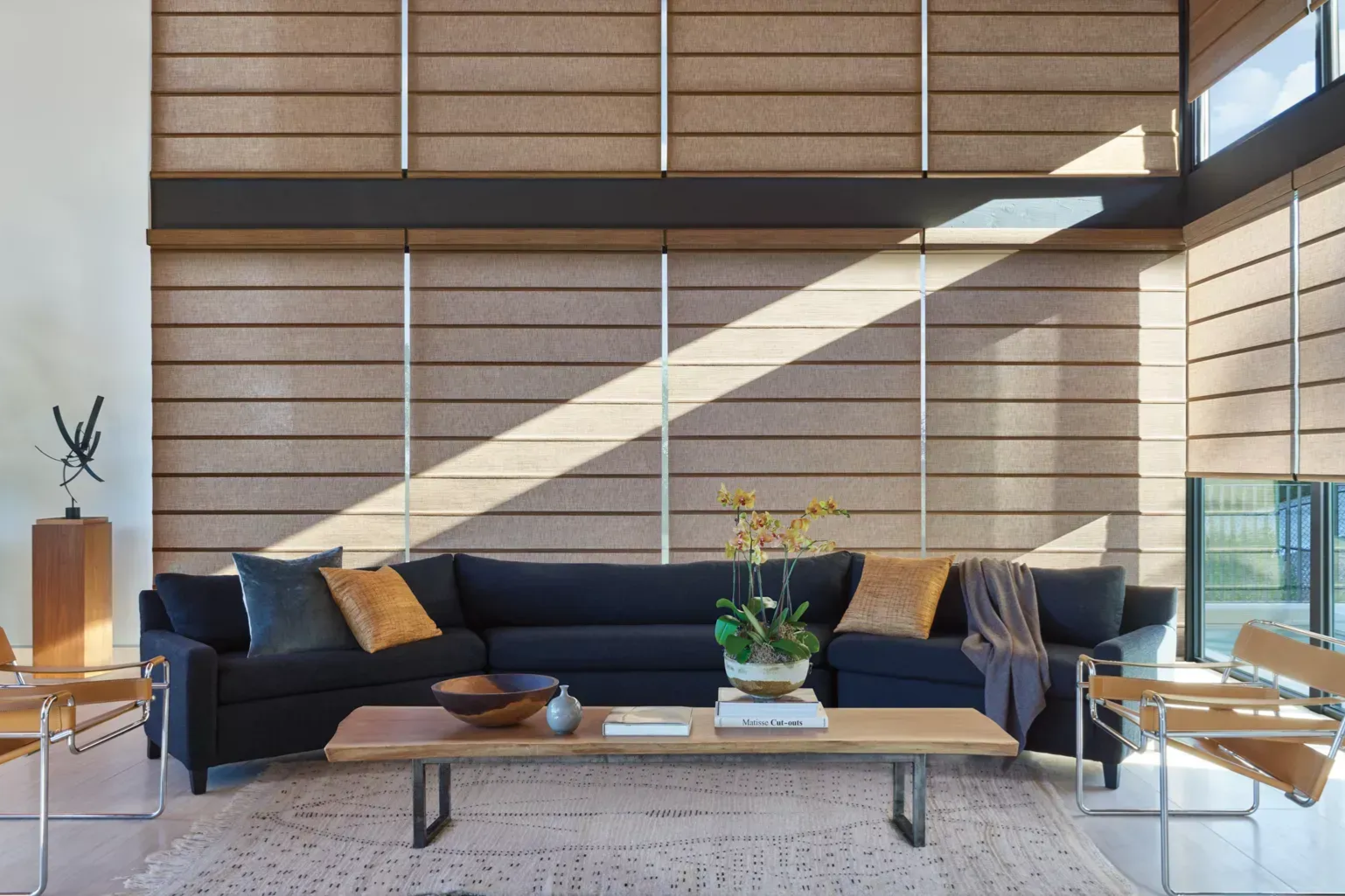 Living room with navy sofa, light wood coffee table, beige rug, and large windows with blinds.