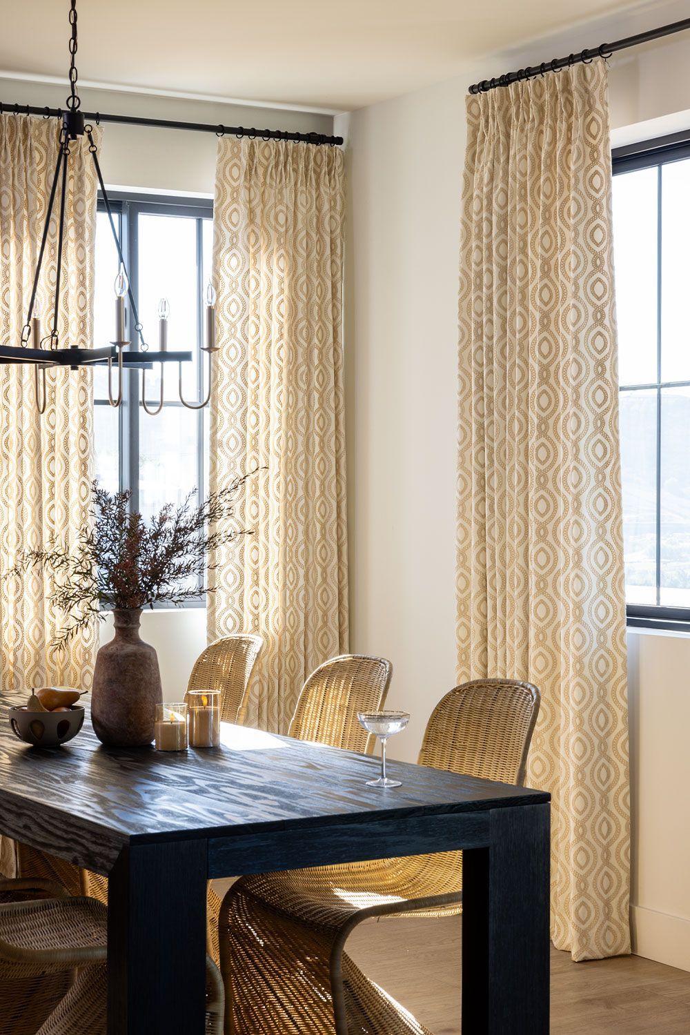 Dining room with black table, wicker chairs, patterned curtains, and a chandelier.