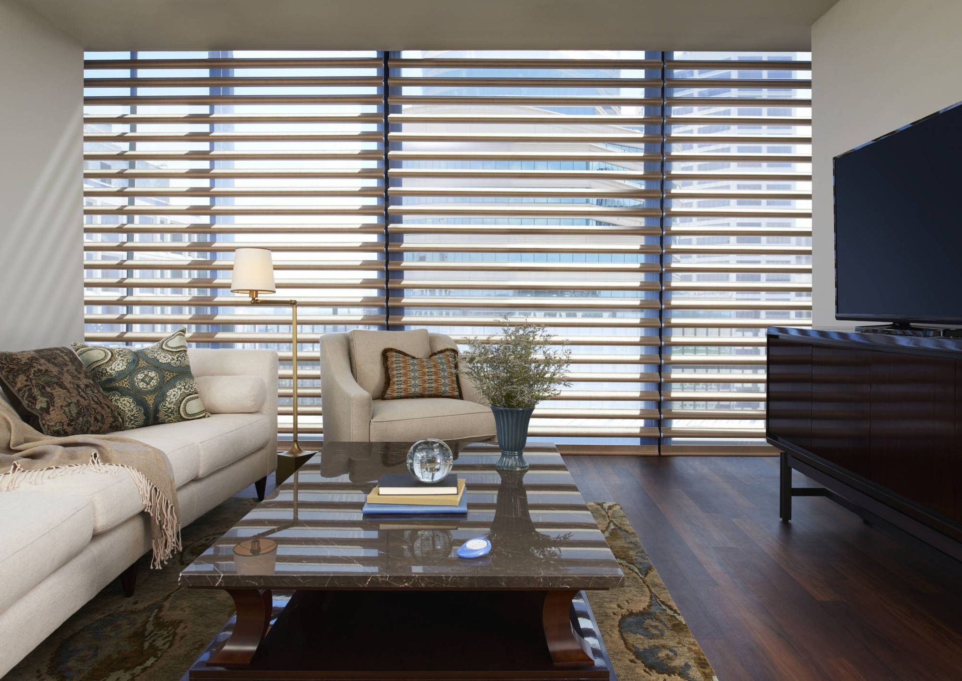 Living room with large window blinds, sofa, armchair, coffee table, and television.