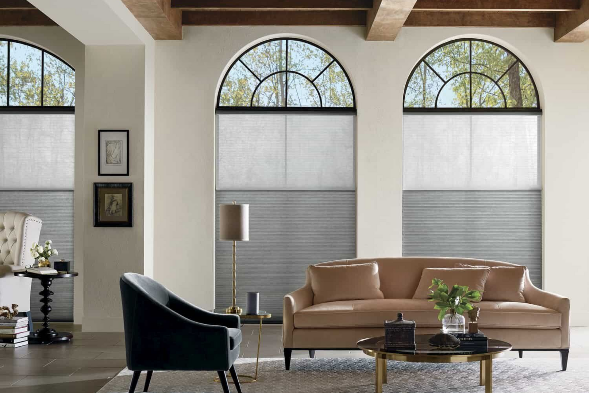 Living room with arched windows, light-colored walls, tan sofa, dark chair, and sheer window coverings.