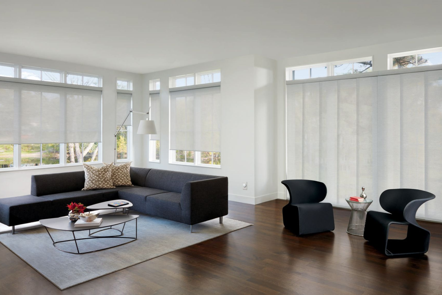 Modern living room with dark gray sectional sofa, panel blinds, and hardwood floors.