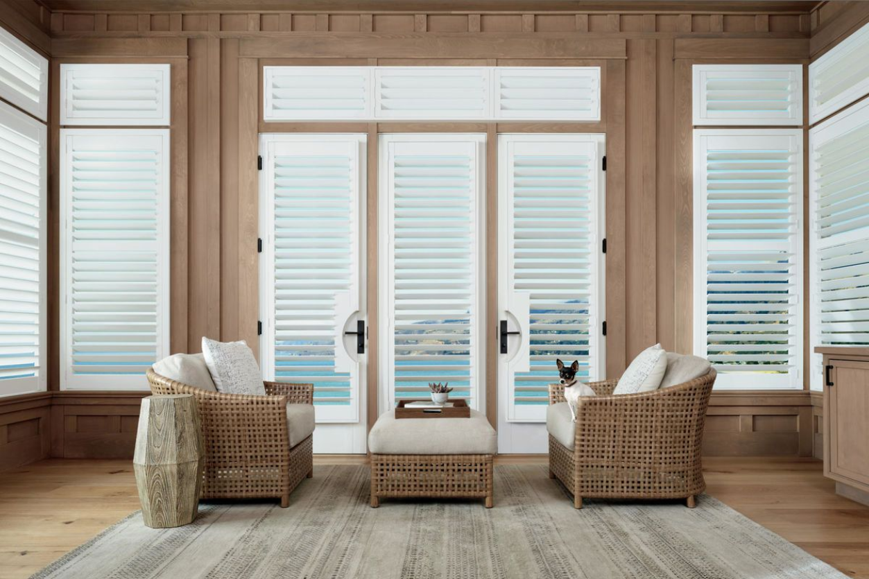 Living room with white shuttered doors and windows, wicker chairs, and ocean view.