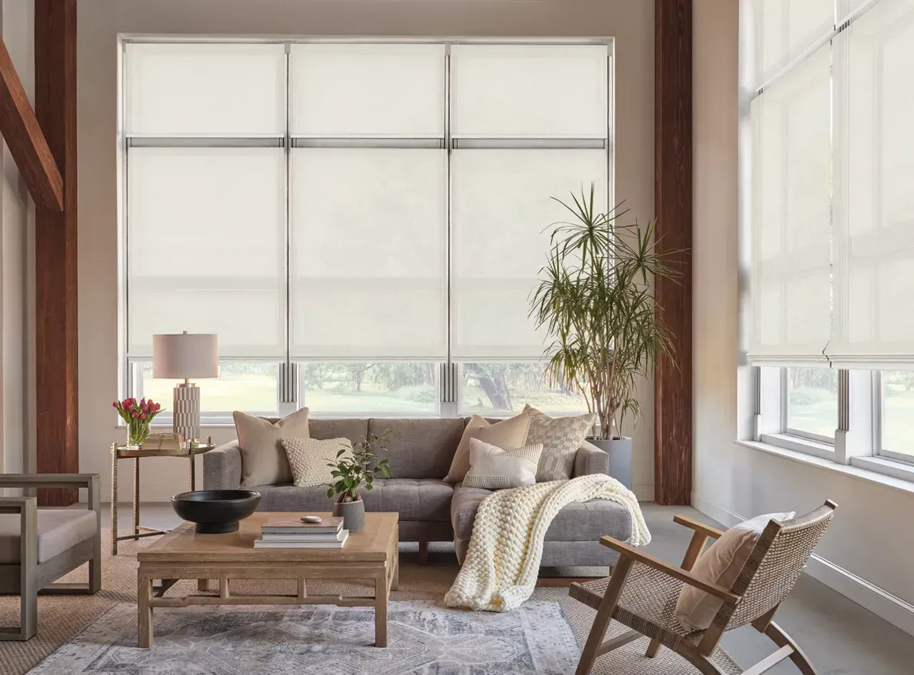 Living room with large windows, light neutral furniture, and roller shades.