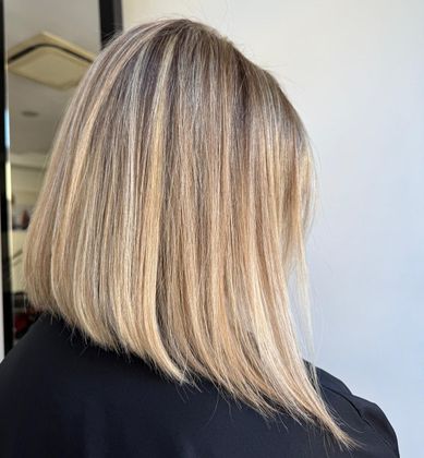Caschetto biondo lungo fino alle spalle, con radici più scure, visto da dietro davanti a una parete chiara.