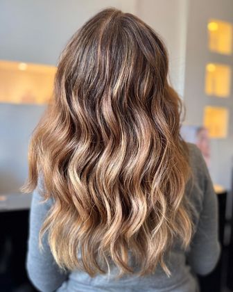Vista posteriore di lunghi capelli castani mossi con mèches bionde in un salone di parrucchieri
