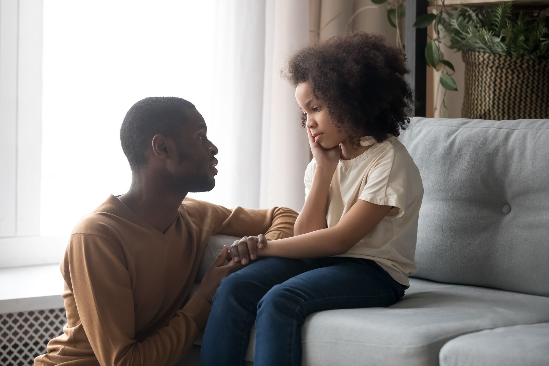 A woman is sitting on a couch talking to a little girl.