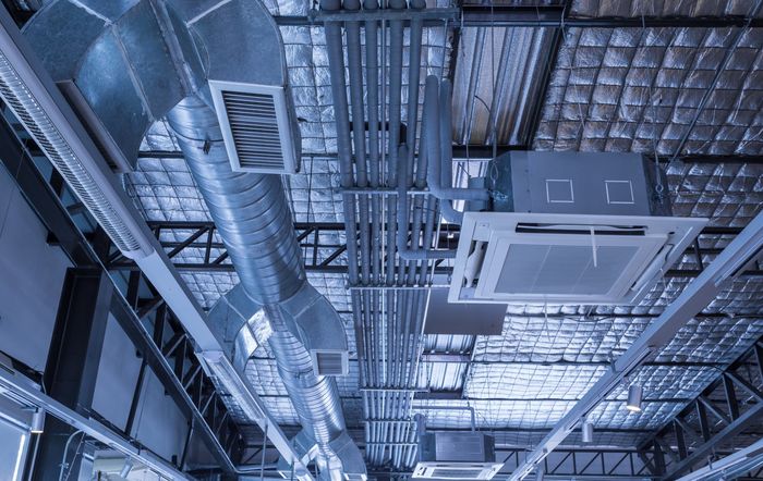 Vue aérienne des conduits de ventilation et des unités de climatisation fixées au plafond d'un bâtiment commercial ou industriel.
