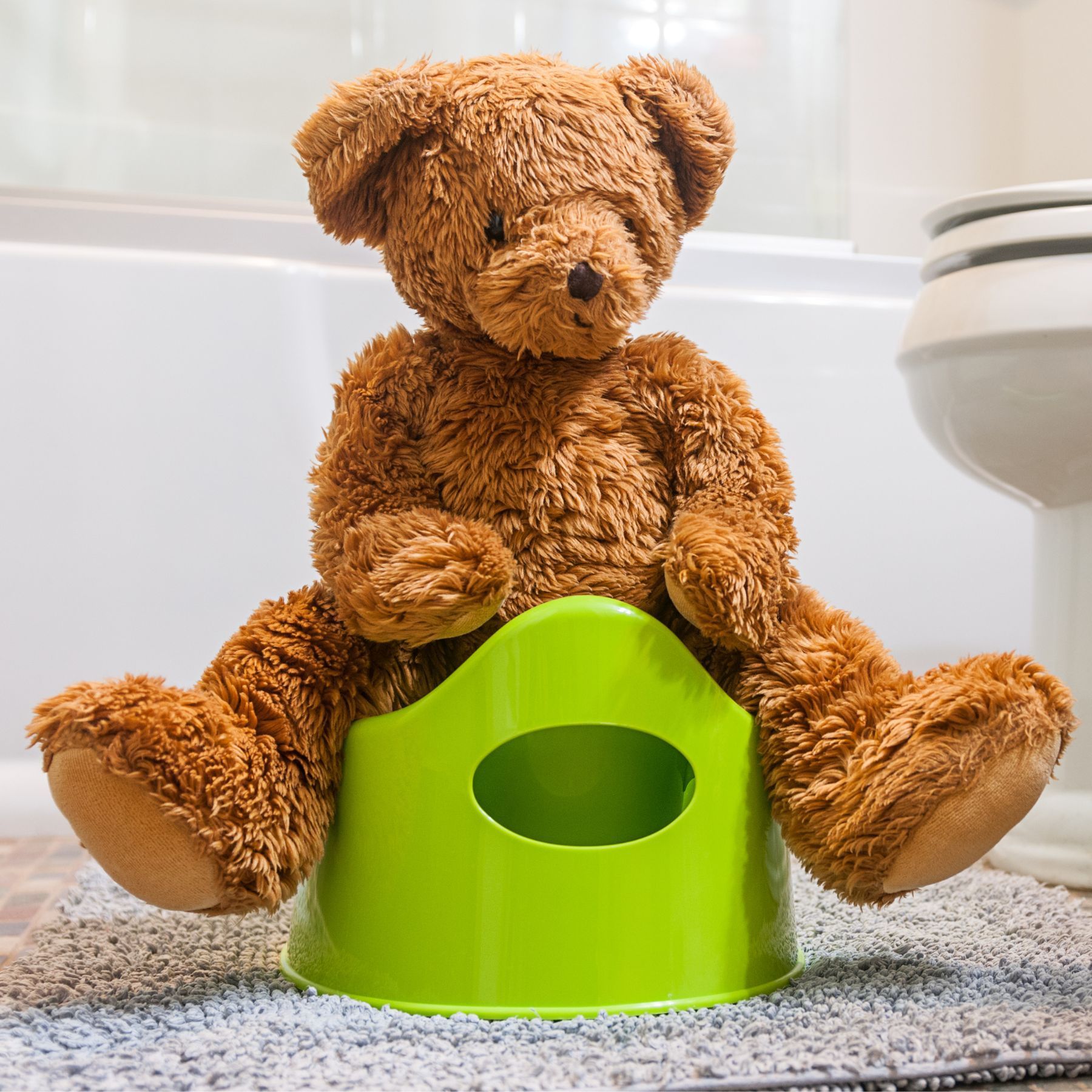 A teddy bear is sitting on a green potty next to a toilet.