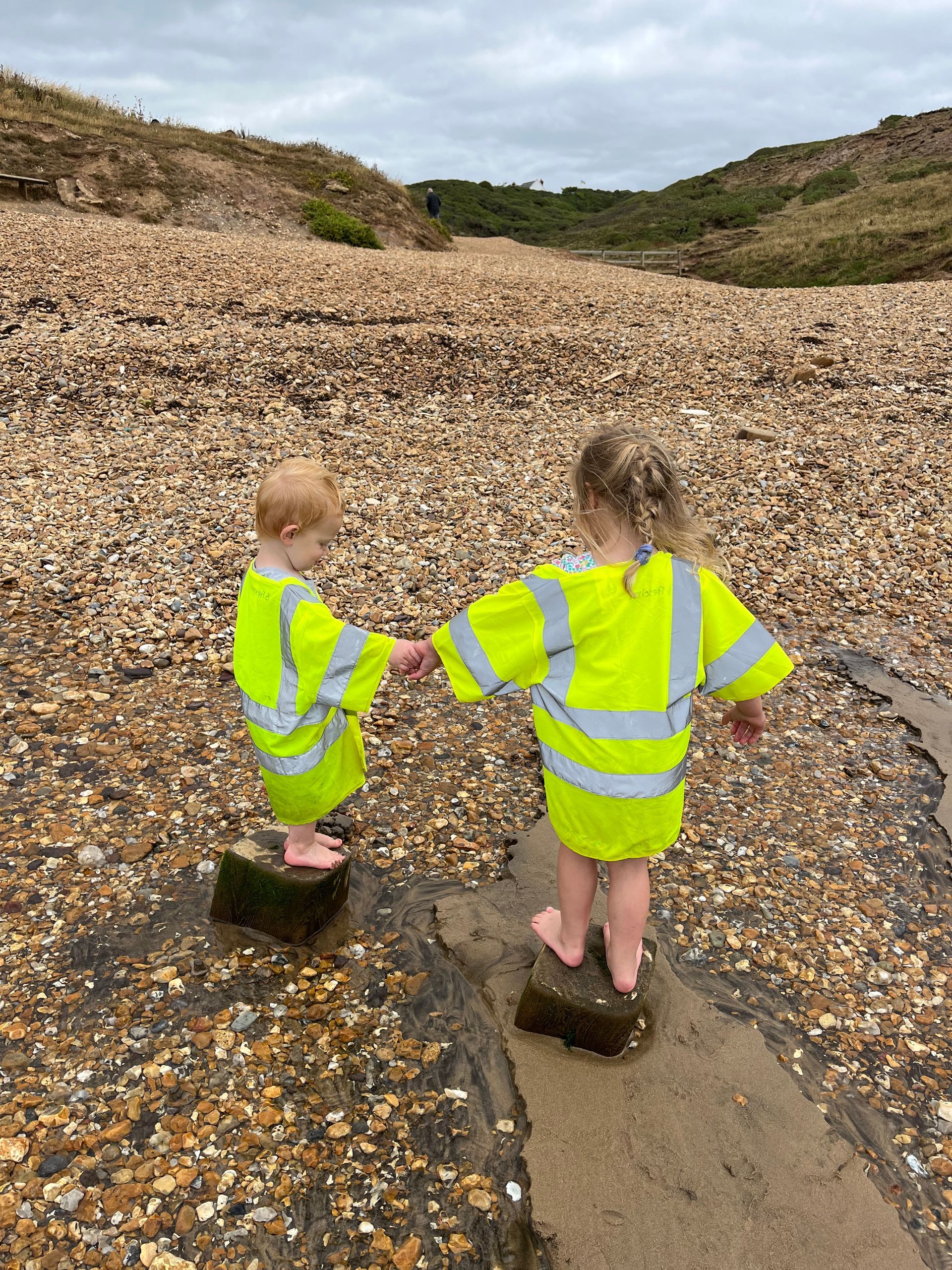 Two little girls are standing on rocks on a beach holding hands.
