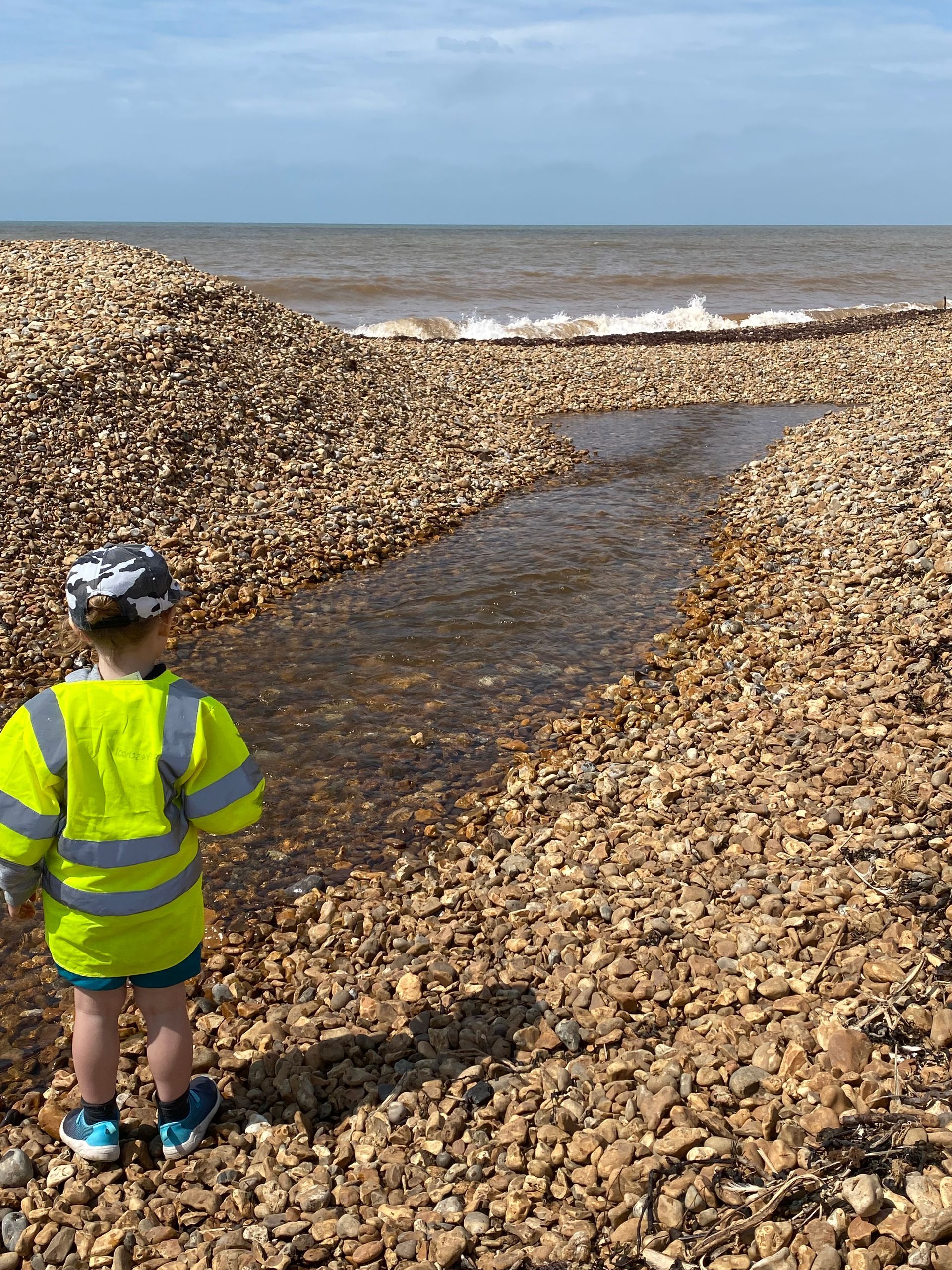 A little boy is standing on a rocky beach looking at the ocean.