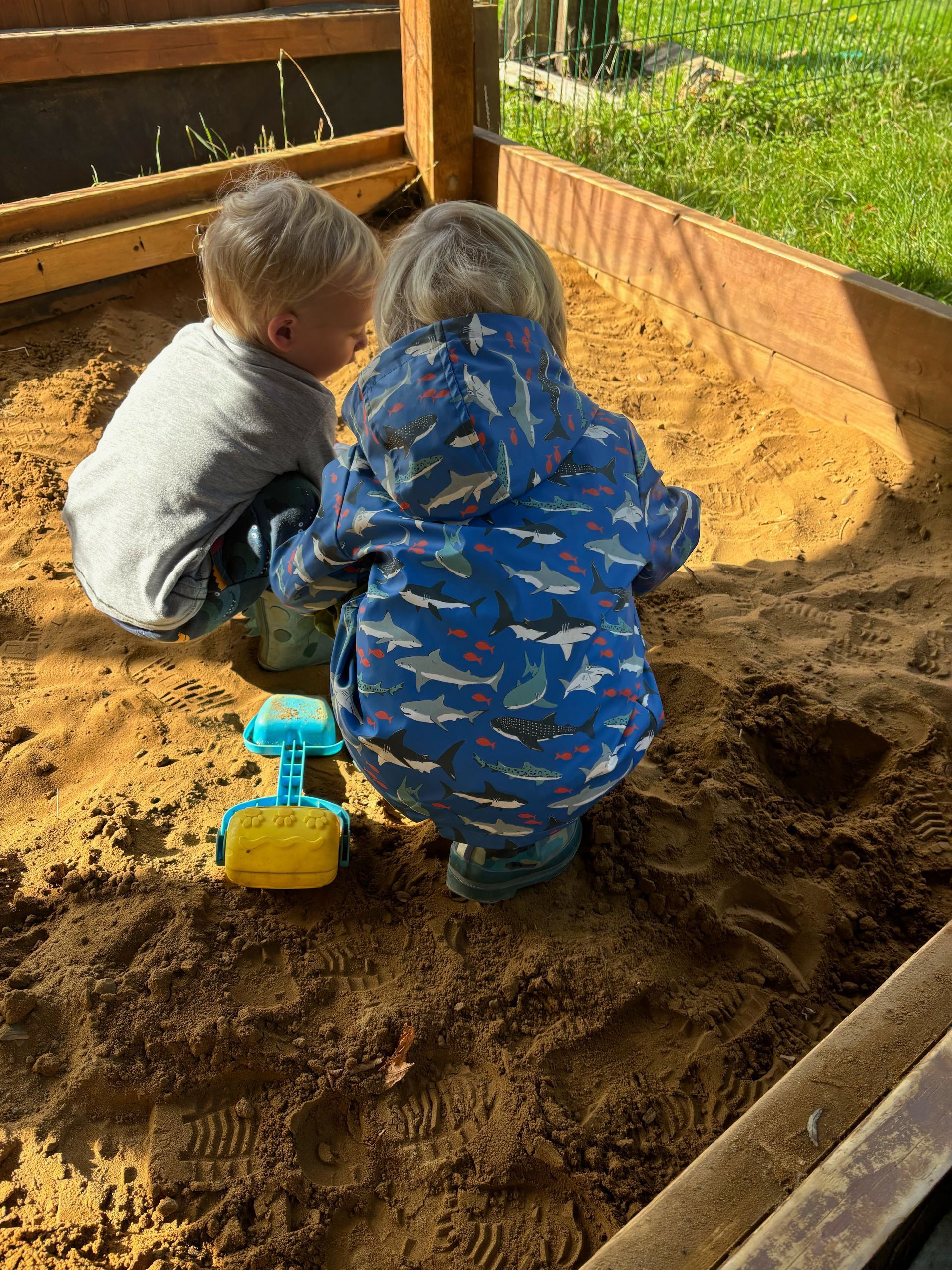 Two young boys are playing in a sandbox.