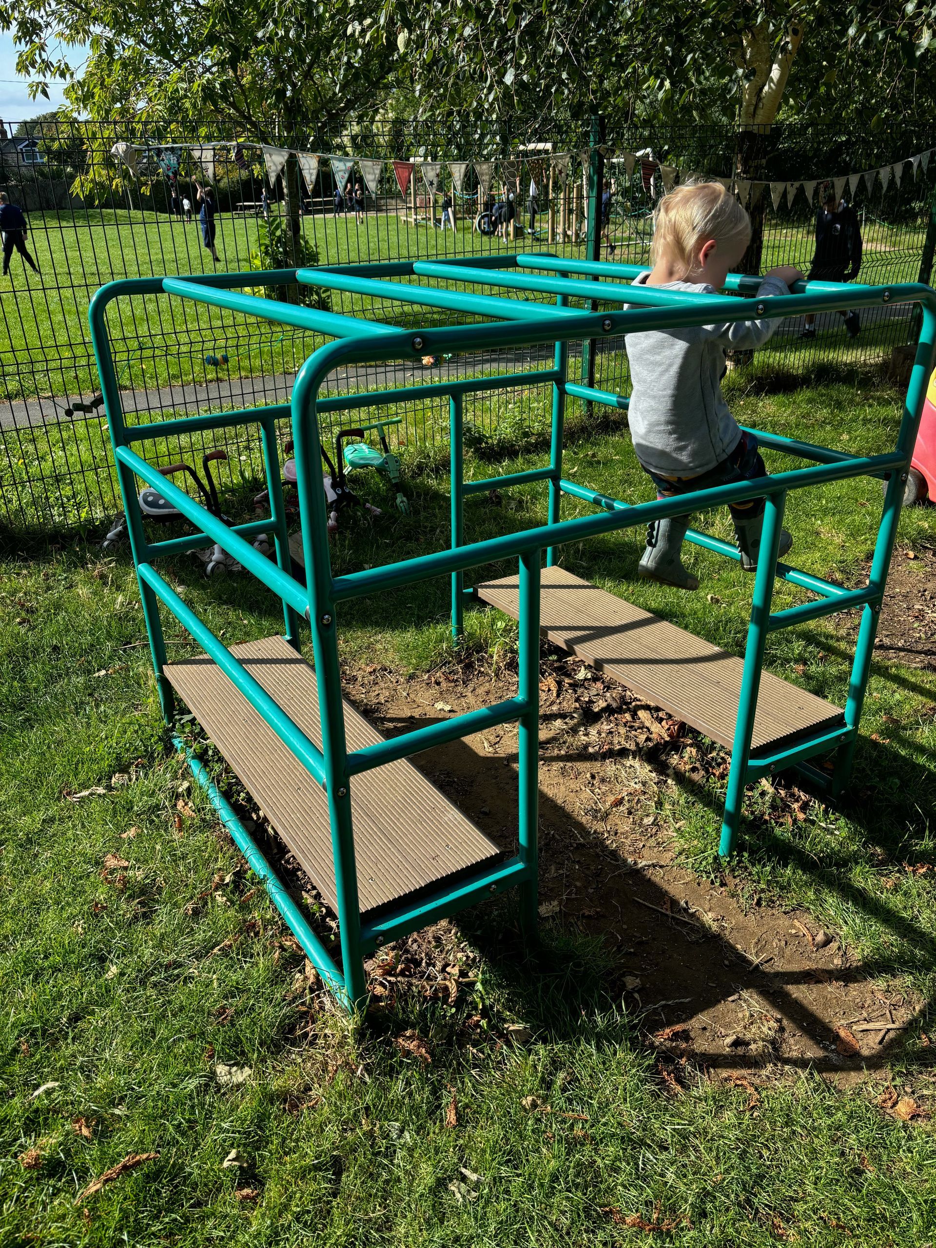 A little boy is playing on a green metal structure in a park.