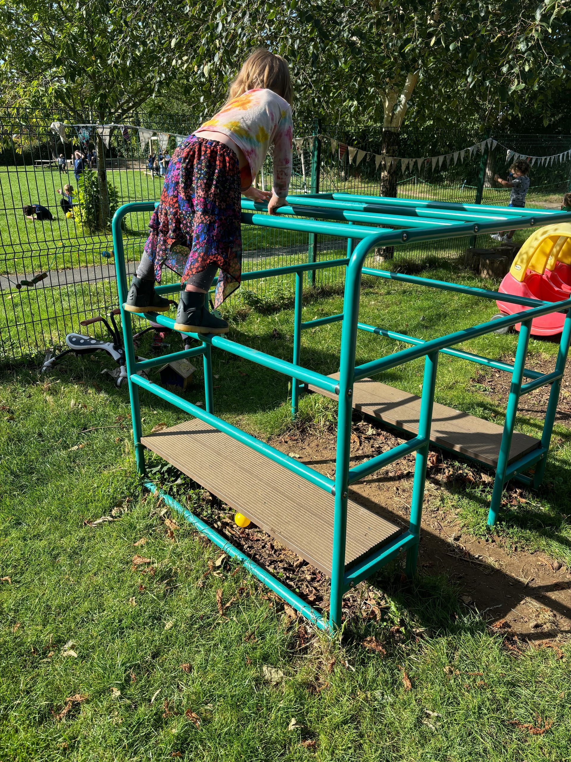 A little girl is playing on a monkey bars in a park.
