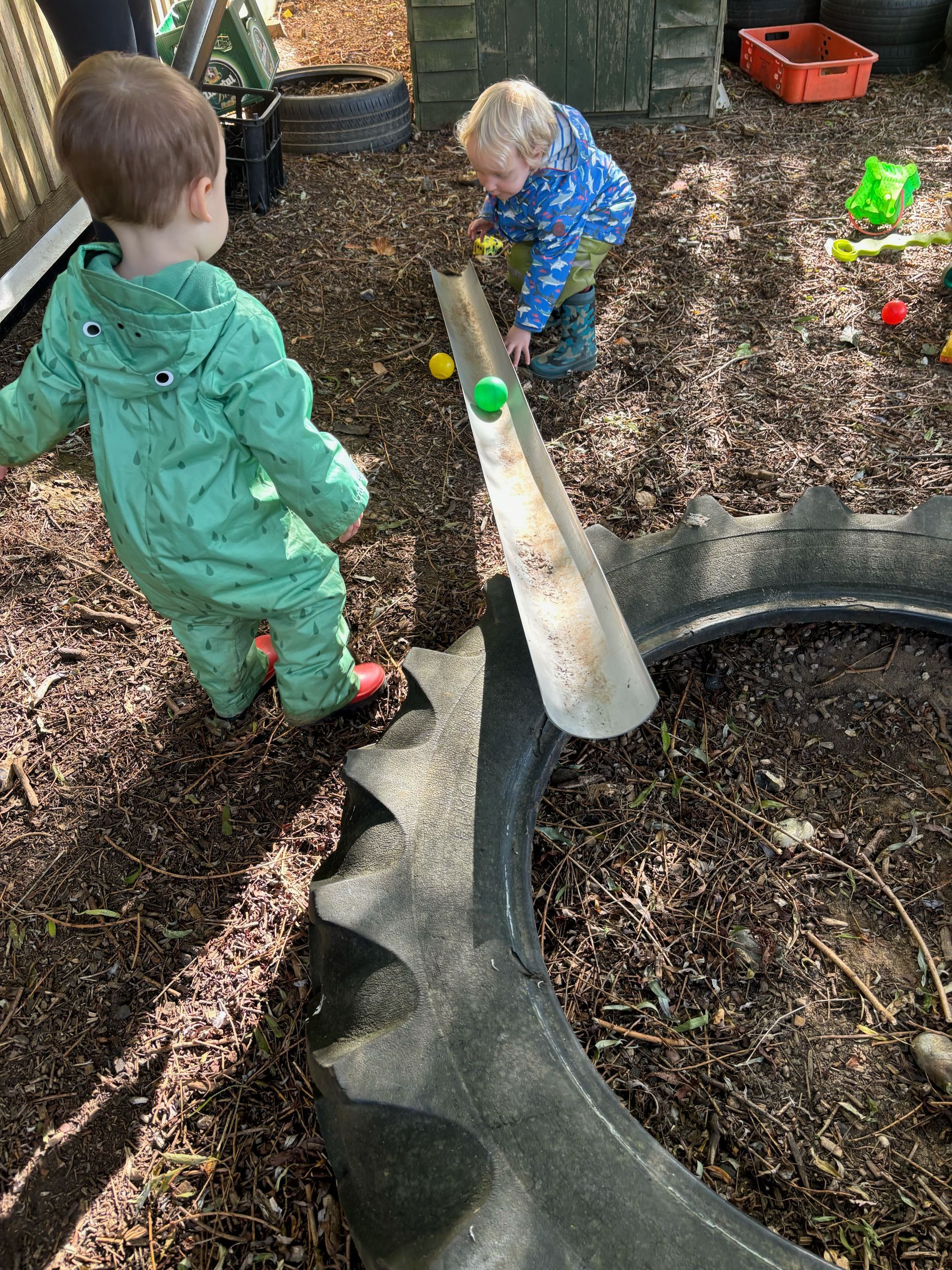 Two young boys are playing with balls in a tire.