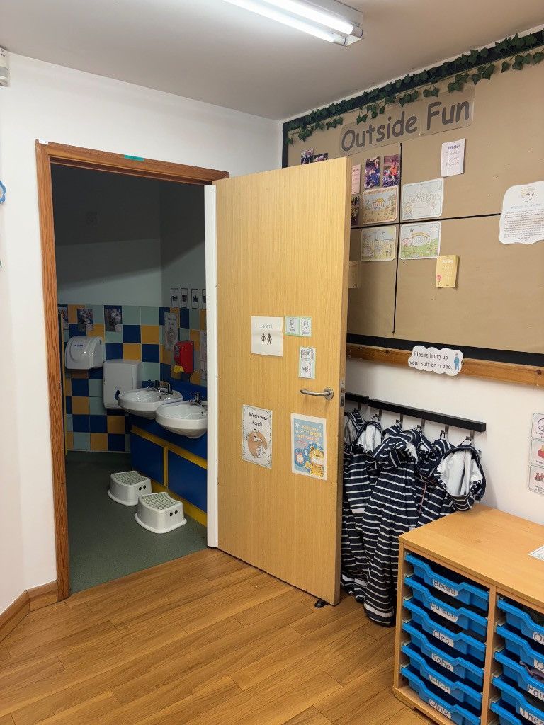 A child's classroom doorway opens to a restroom with blue and yellow tiles.
