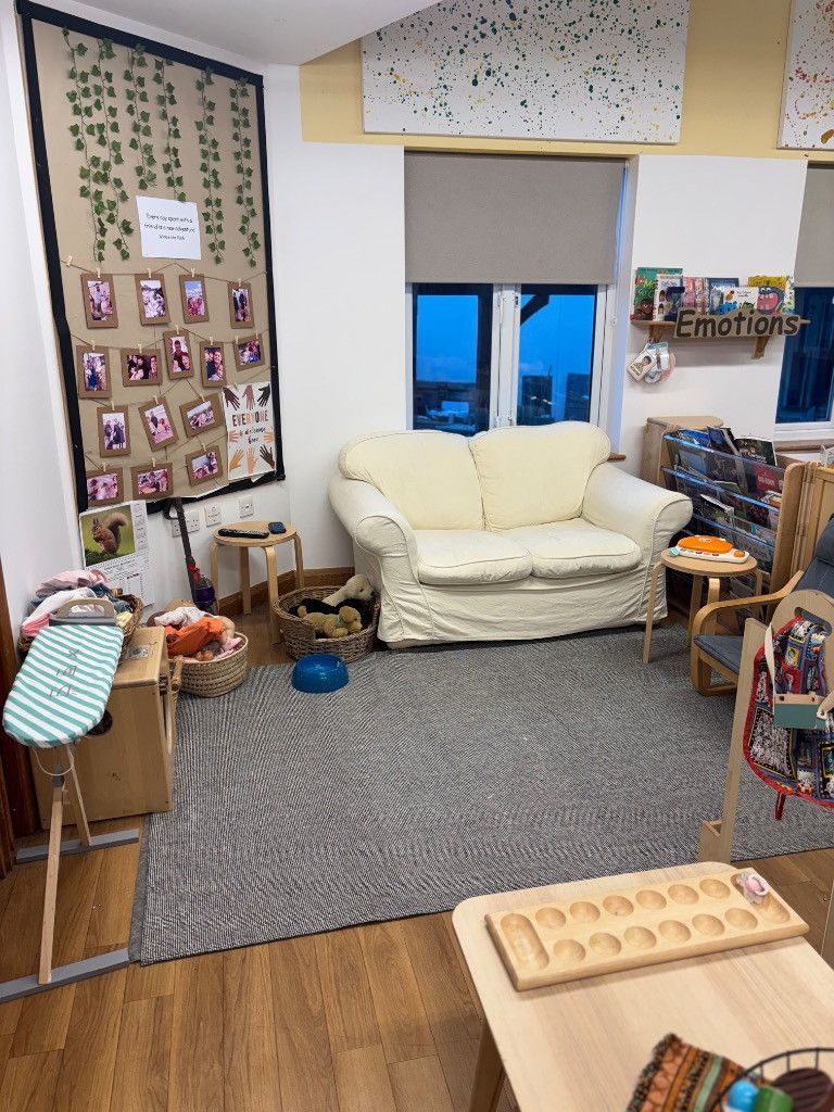 Cozy room with a couch, rug, play area, photos on wall, and window with a twilight view.