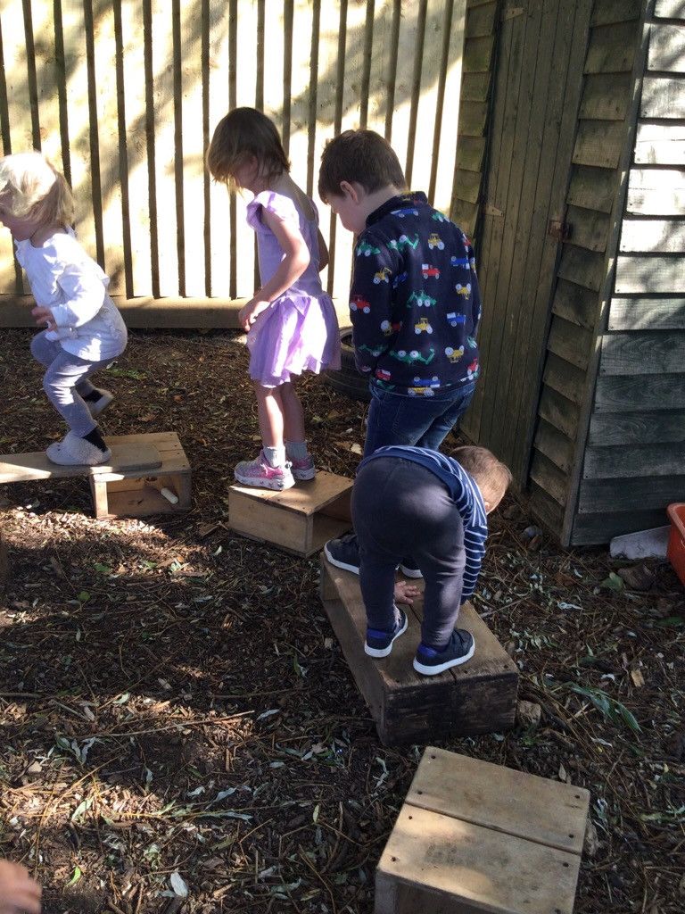 A group of children are playing on wooden blocks outside.