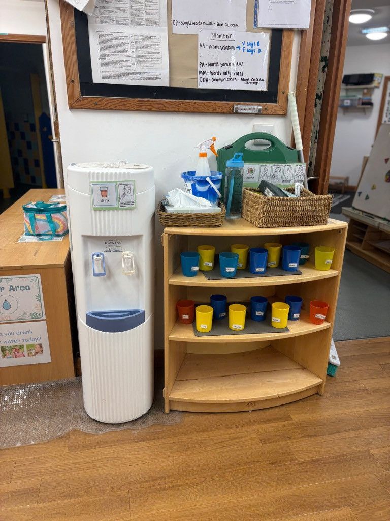 Water cooler and wooden shelf with colorful cups in a classroom setting.