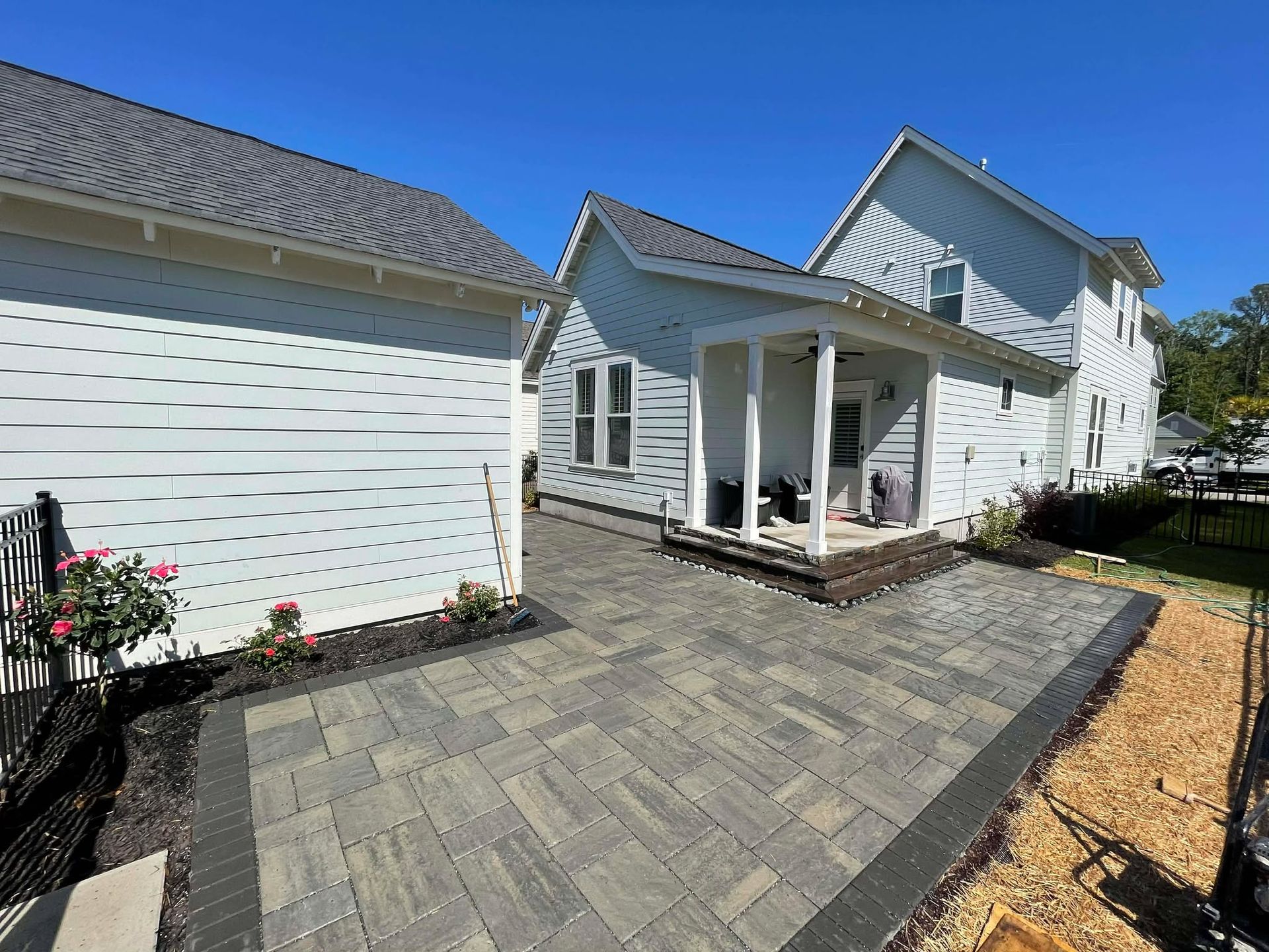 Paver patio with a white house and attached garage under a bright blue sky.