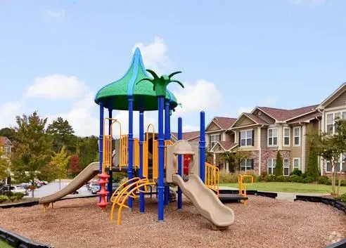 Playground with slides and colorful structures, with apartment buildings in the background.