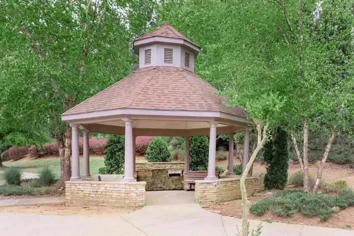 Gazebo with outdoor seating and grill area in a park-like setting.