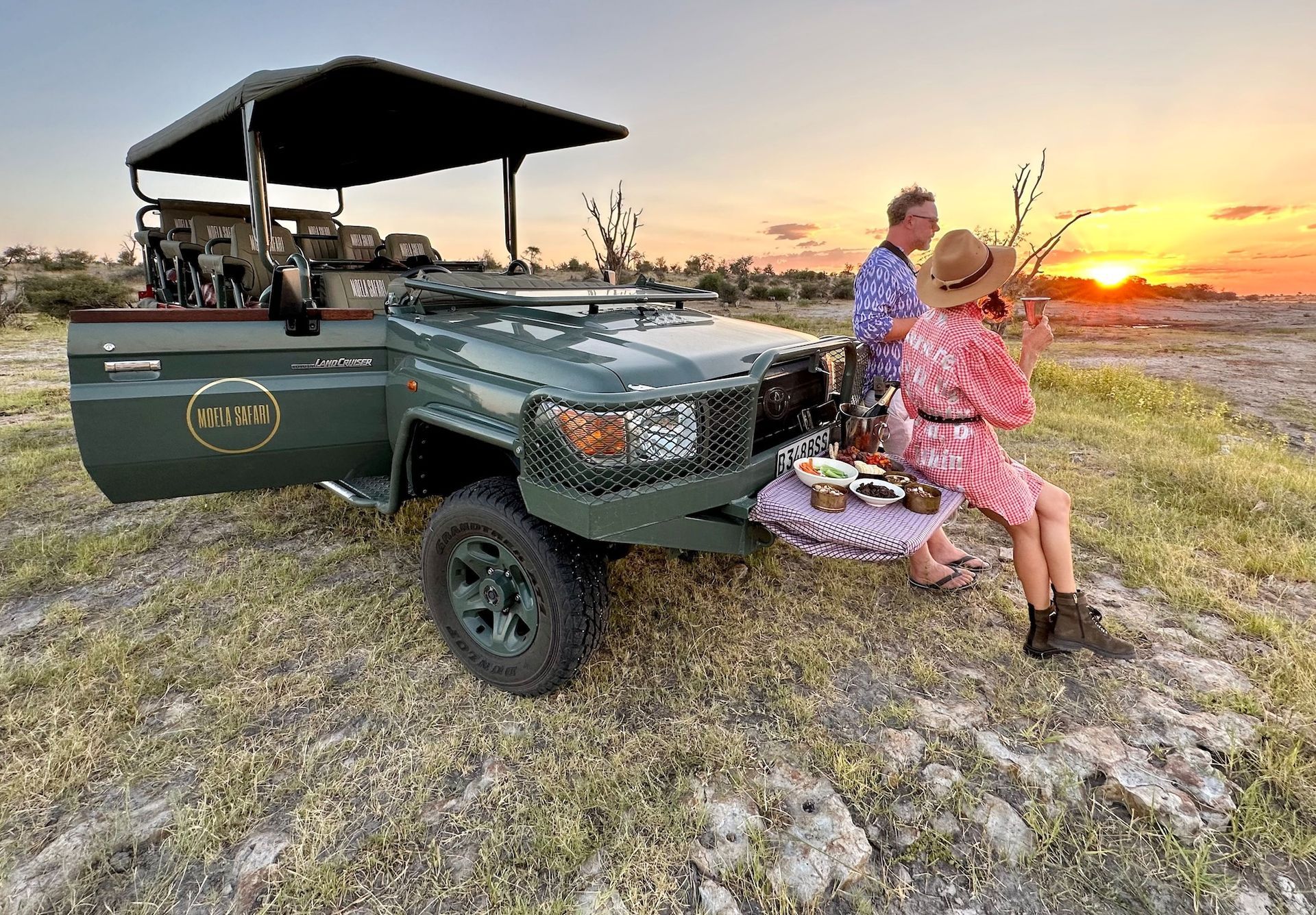 Green safari vehicle parked at an outdoor event with people gathered in the background.