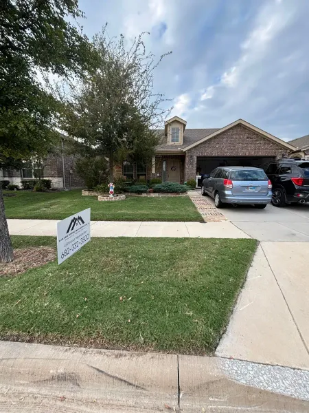 A single-story brick house with a front lawn, a driveway containing two parked SUVs, and a yard sign in the grass.