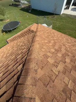 An overhead view of brown asphalt roof shingles on a house, with a green yard and trampoline visible below.
