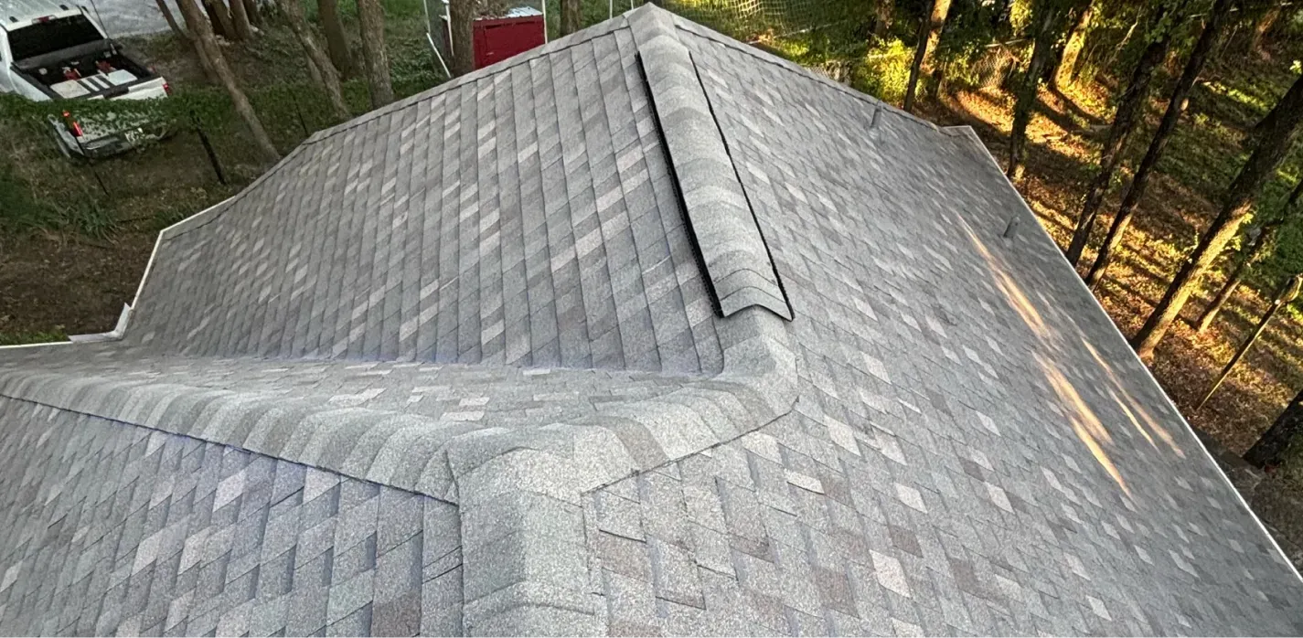 An elevated view of a residential roof covered in gray asphalt shingles, showing a ridge vent and a hip roof design.