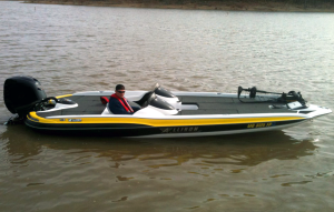 Bass boat on water with person at the helm. Yellow and black trim.
