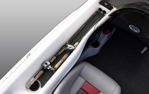 Fishing rods secured in a boat's side-mounted rod holder, near the steering wheel and passenger seat.