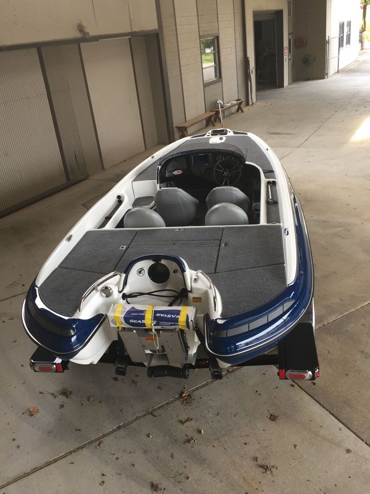 Bass boat, white and blue, on trailer, parked under an overhang.