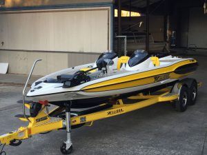 Yellow and white speed boat on a matching yellow trailer, parked on a concrete surface.