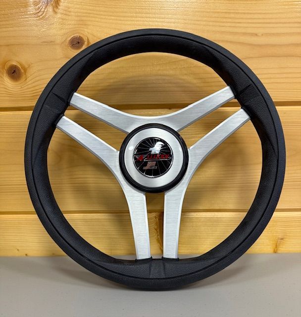 Silver and black three-spoke boat steering wheel with eagle logo on a wood background.