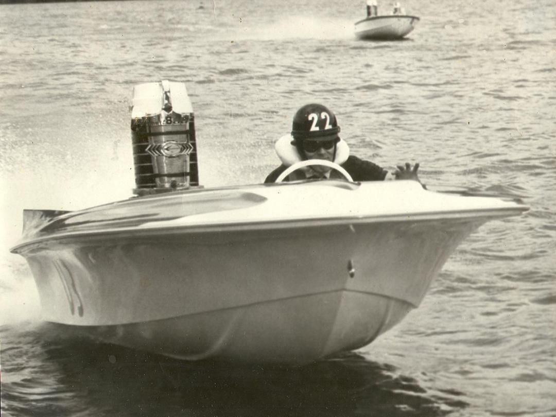Vintage speedboat with driver wearing helmet, racing on water, number 22 on the helmet.