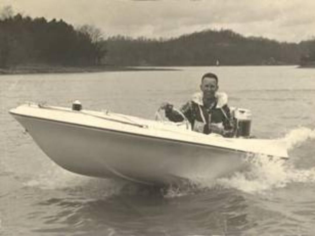 Man driving a white motorboat on a lake, water splashing.