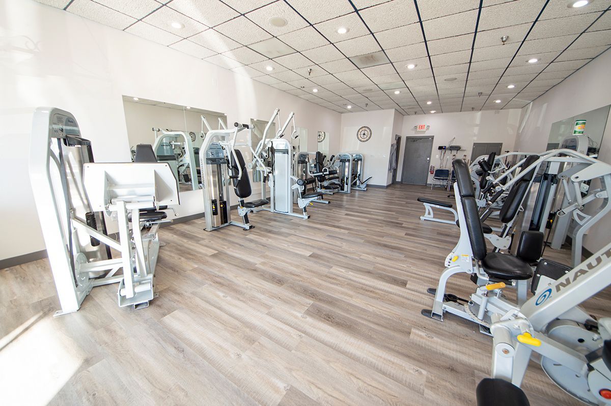 Bright, empty gym with exercise machines, wood floors, and large mirrors along the wall