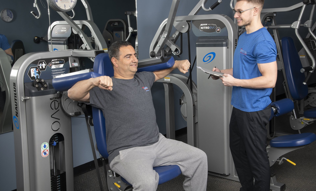 A Man is Sitting on a Machine in a Gym While a Man Talks to Him | Uniontown, OH | My Personal Trainer