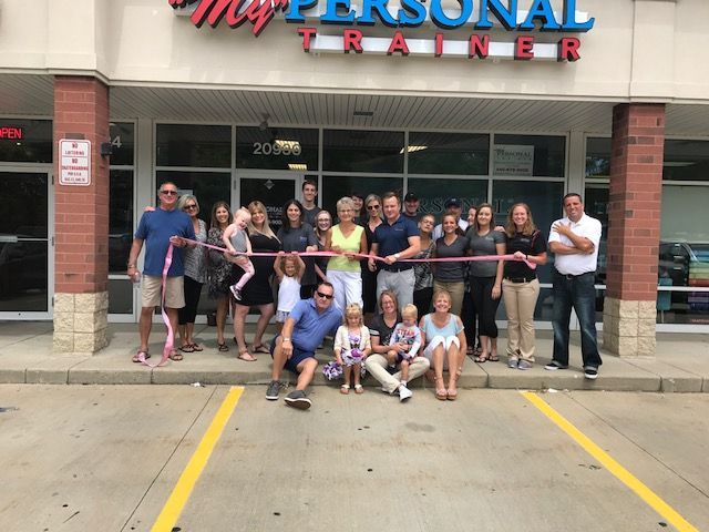 Group posing outside My Personal Trainer storefront, holding a ribbon in front of the entrance.