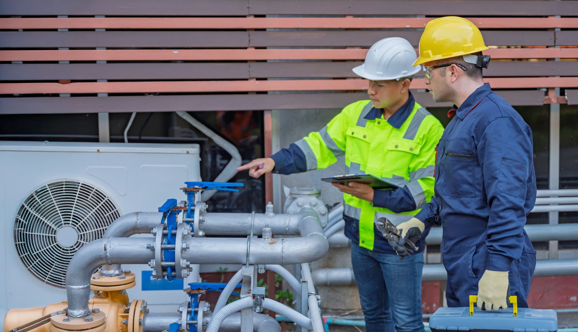 hvac contractor inspecting industrial HVAC unit and pipes with technicians in hard hats.
