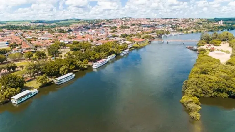 Vista aérea de uma pessoa flutuando em uma piscina natural de cor turquesa brilhante, cercada por vegetação tropical exuberante.